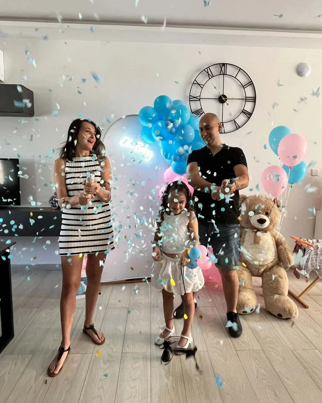 Family celebrating a balloon-filled gender reveal with blue confetti
