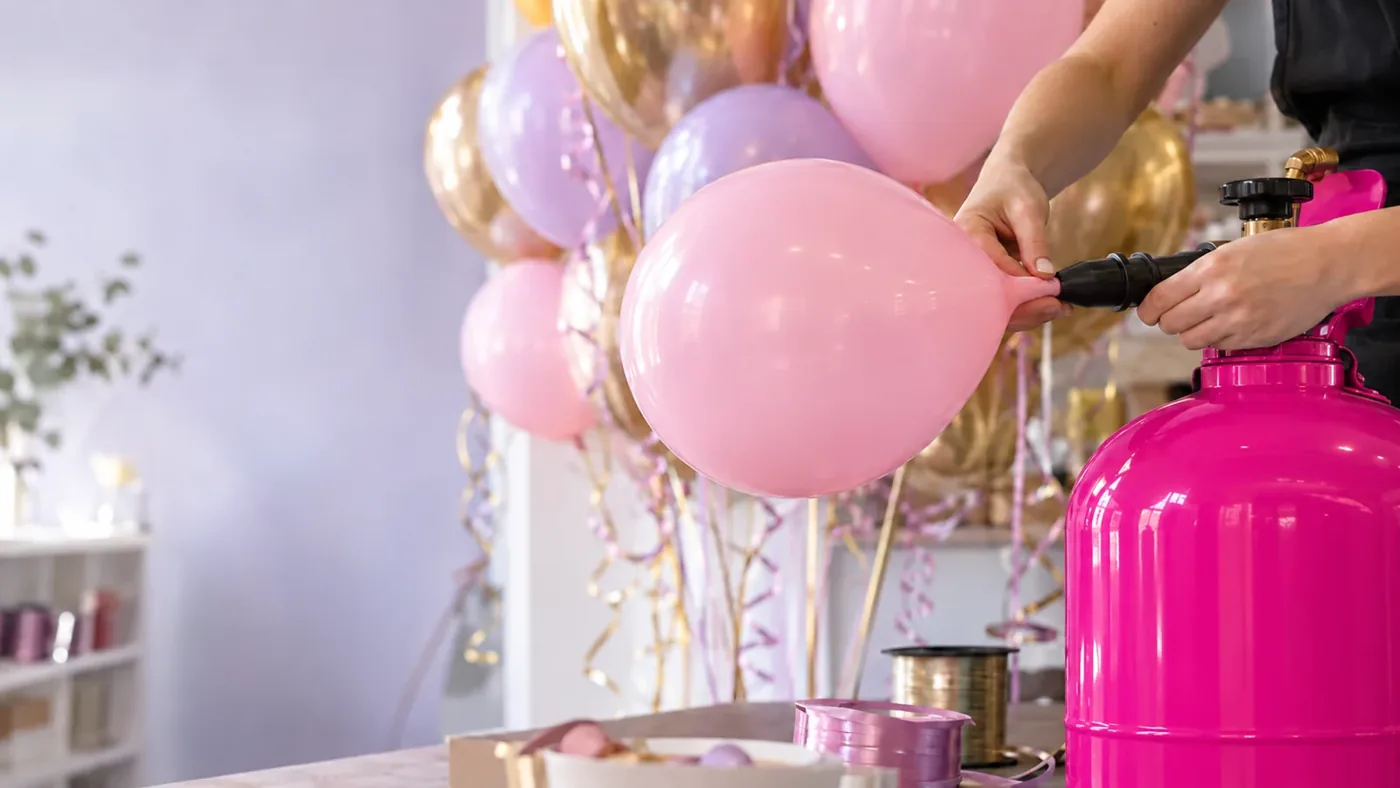 Shop assistant inflating a balloon at a PartyMalta pink helium cylinder