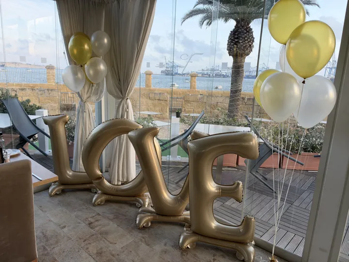 Gold LOVE letter balloons and white and gold helium bouquets beside a sea view